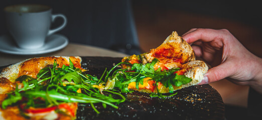 woman Hand takes a slice of Pepperoni Pizza with Mozzarella cheese, salami, Tomatoes, pepper, Spices and Fresh arugula