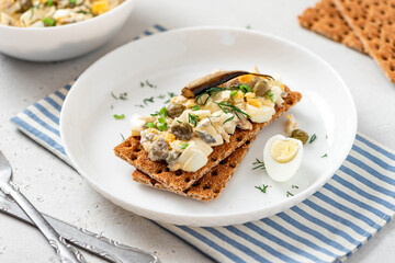 Egg salad with anchovies on crispy bread. Sandwich with Swedish egg salad gubbröra in a plate on a white concrete background close-up. Scandinavian cuisine.