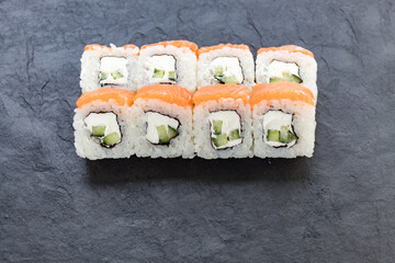 Rolls with salmon on a black stone board. Serve a cutaway dish. Rice, avocado, salmon