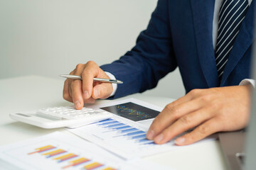 A close-up of an Asian male finance man's hand pressing a calculator on a desk in an office.