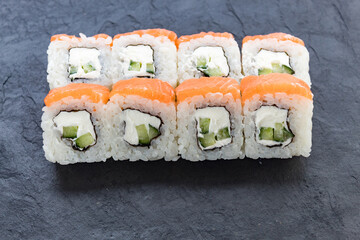 Rolls with salmon on a black stone board. Serve the dish. Rice, fish, avocado.