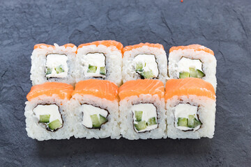 Rolls with salmon on a black stone board. Serve the dish. Rice, fish, avocado.