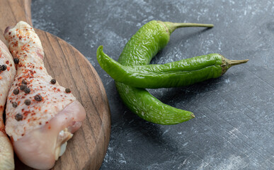 Fresh organic chicken drumsticks and green pepper on wooden chopping board 