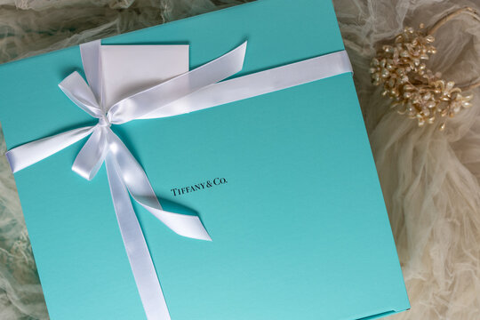 Flourtown, PA - Feb. 22, 2021: Tiffany gift box with white satin ribbon and gift card on a background of soft focus faded antique wedding veil with pearl headpiece