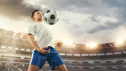 Junior football or soccer player at stadium in flashlight. Young male sportive model training....