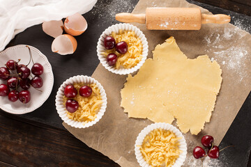 Homemade baking cherry cake ingredients - bowl, flour, eggs and fresh berries on rustic dark table
