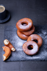 Donuts with powdered sugar and a cup of coffee. Traditional donuts in the shape of a ring fried in oil, on a black background. Junk food. Close-up.