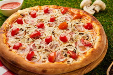 Traditional italian Pizza with ham, mushrooms and onion on green grass background