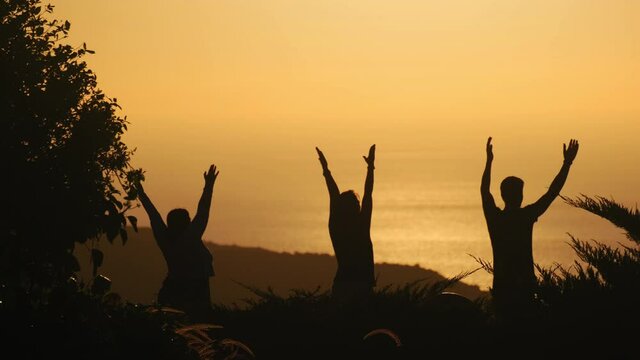 Silhouettes of three yogis doing mountain pose while facing the ocean at sunset