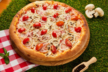 Traditional italian Pizza with ham, mushrooms and onion on green grass background