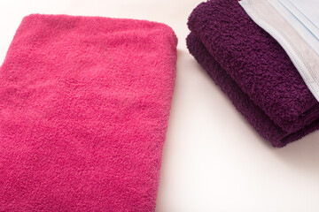 Rose and violet towels on white background, hygiene masks on bath towels
