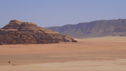 Fototapeta na wymiar Einsamer Jeep fährt durch die Wüste Wadi Rum, im Hintergrund Filmkulisse Lawrence von Arabien