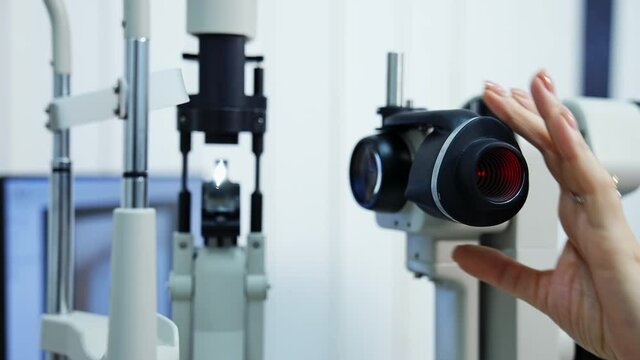 Panning shot of female ophthalmologist`s hand doing eye exam with slit lamp. Preparing special technic for checking eyesight. Selective focus.