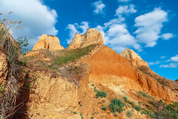 Landscape view clay cape cliffs. Green grass, lawns grown on slopes of clay mountains against blue sky. Hills of mountain and slopes of cape are overgrown with half grass and plants. Clay wall