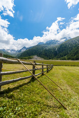 Fototapeta na wymiar two agricultural tools on a wooden fence on a alpine pasture with high mountains