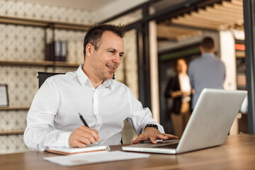 Smiling man working with laptop and taking notes, portrait.