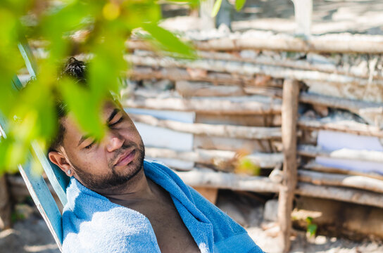 dark-haired latin man from the dominican republic resting his day off on the beach with a towel and sleeping