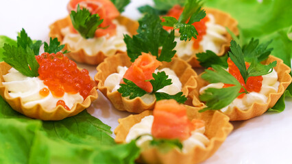 Salmon fillet mini tartlet with cream, garnished with red salmon caviar on a white plate with herbs on the table Side view