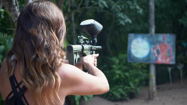 An active woman with a paintball gun practices shooting at a target - concept: frustration, anger, revenge, relationship, breakup, ex boyfriend