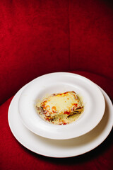 Portion of delicious Italian Lasagne in a deep and round plate on a red background