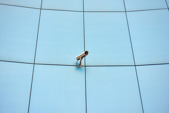 A dirty security camera hangs on the wall of the building.