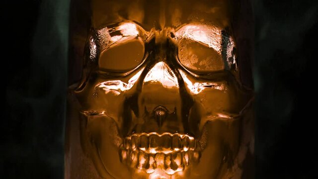 Brown Skull Boils Poisonously. Bright, rich gold glass vessel in the form of the skull, from which are evaporation and slow down the edges on a black background