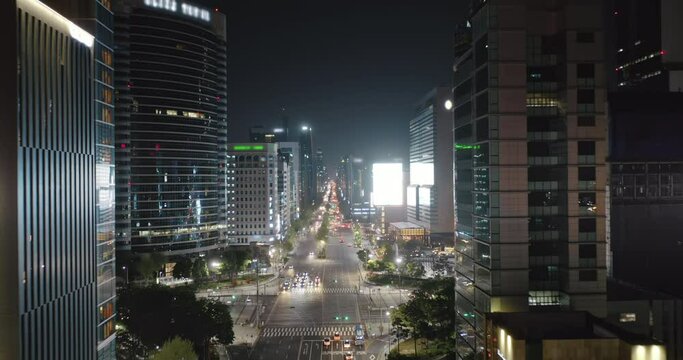 View from above to Seoul Gangnam District on the night. Camera moving backwards between modern skyscrapers showing beautifully illuminated city with busy streets, traffic and futuristic buildings. 