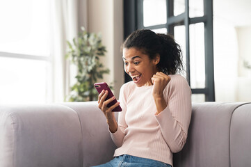 Excited mixed-race teenage girl celebrating success, winner of the competition showing hand fist...