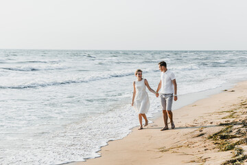 Fototapeta na wymiar beautiful loving couple walks on the seashore. happy young couple spend time on the beach. honeymoon newlyweds. guy with girl at dawn of the day. couple on vacation. summer rest. couple hugging
