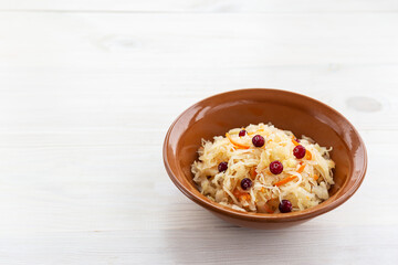 Sauerkraut with cranberries in a clay bowl. Russian traditional food. Horizontal orientation, copy space.