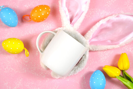 Easter product mockup with bunny ears and easter eggs on pink background flatlay. White coffee mug mock up with negative copy space for your text or design here.