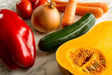 Close up shot of red pepper, pumpkin, zucchini, tomatoes and carrots on marble table in the kitchen. Fresh vegetables in the kitchen. Healthy and vegan food.