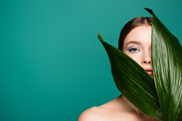 sensual young woman looking at camera near wet leaf isolated on green