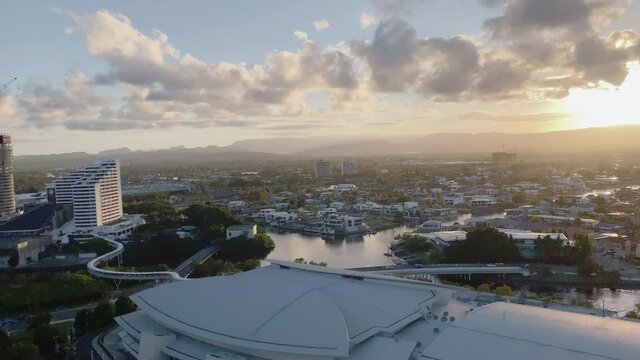 4K UHD Panning View of Casino construction, Convention Centre on the Nerang River at sunset in downtown Broadbeach district, Gold Coast Australia, aerial view. Commuter Tram, Gold Coast beach life.