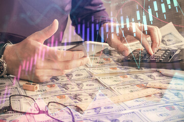 Double exposure of man's hands holding and using a digital device and forex graph drawing. Financial market concept.