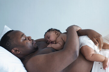 Father lying on bed holds his baby daughter, 4 mouth baby on his chest, man is not wearing a shirt