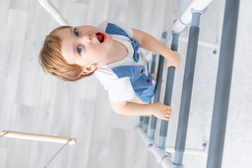 a child on the Swedish wall plays sports at home, a boy climbs a ladder with a rope, the concept of sports and health