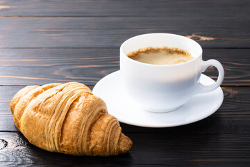 cup of coffee and croissant on wooden table. Top view