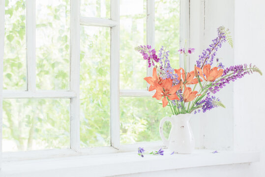lilly and lupine flowers in jug on windowsill