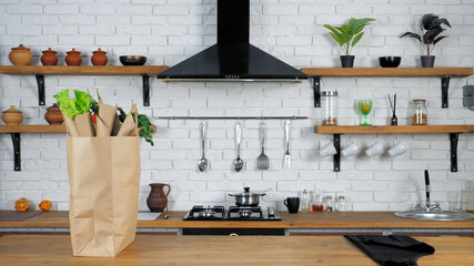 Black apron and paper bag with fresh vegetables ingredients for cooking delicious salad stands on table, preparing cook healthy food at home kitchen