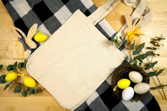 Easter Farmhouse theme product flatlay mockup with buffalo plaid and wood bunnies. Natural canvas cotton Easter Egg Hunt tote, shopping bag with negative copy space for your text or design here.