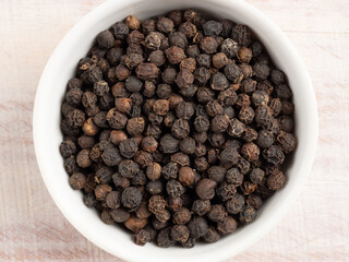 Spice black pepper in a white bowl on a light wooden background