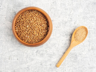 Buckwheat in a wooden cup, salt in a spoon on a white concrete background