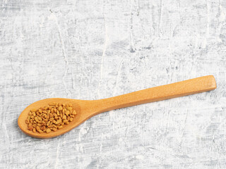 Spice fenugreek in wooden spoon on a white concrete background