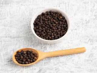 Spice black pepper in ceramic bowl and wooden spoon on a white concrete background