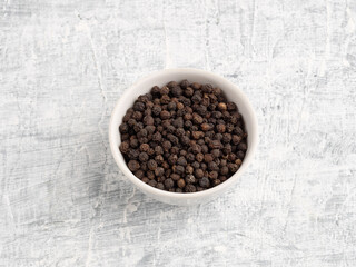 Spice black pepper in ceramic bowl on a white concrete background