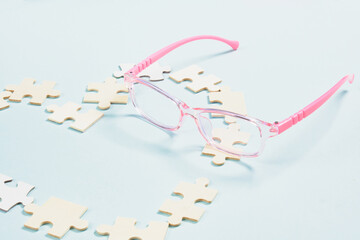 childish pink glasses and a heart made of wooden puzzles on a blue background, glasses for small children