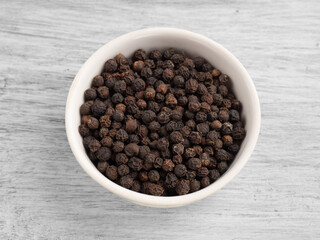 Spice black pepper in ceramic bowl on white wooden background