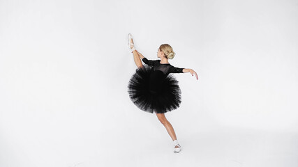 Naklejka premium flexible ballerina in tutu skirt and pointe shoes stretching while dancing on white background