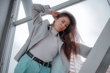brunette with a Japanese appearance in a light sweater and a gray jacket and jeans against the backdrop of the city
